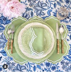 a place setting with green and white plates, silverware and pink peonies