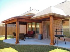 a covered patio with chairs and grill in the back yard, next to a brick building