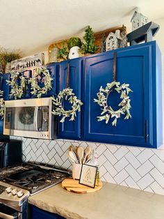 a kitchen with blue cabinets and wreaths hanging on the wall above the stove top