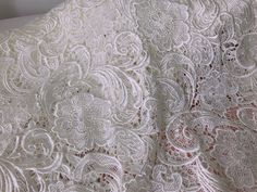 white lace fabric with flowers and leaves on the bottom, as well as an intricate design