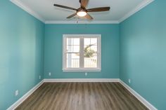 an empty room with a ceiling fan and blue paint on the walls, wood flooring