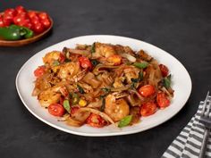 a white plate topped with pasta and shrimp next to a bowl of tomatoes, peppers and basil