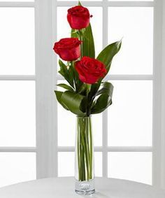 three red roses in a vase on a table