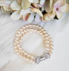 two bracelets with pearls are sitting next to flowers