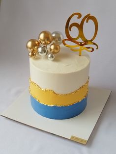 a white cake with gold and blue decorations on top is sitting on a card board