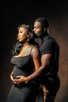 a man and woman standing next to each other in front of a dark background with their arms around one another