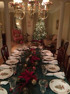 a dining room table set for christmas with plates and silverware on the centerpiece