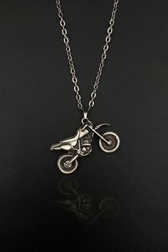 a silver necklace with a motorcycle on it's side and a chain hanging from the front