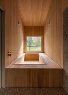 an empty wooden room with a window and bench in the center, surrounded by wood paneling