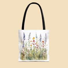 a tote bag with flowers painted on the front and side, sitting against a beige background