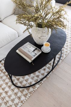 a coffee table with a book, cup and plant on it in front of a couch