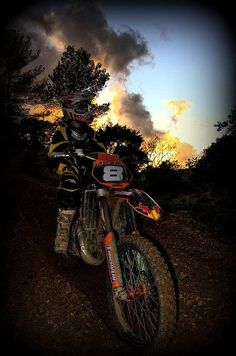 a dirt bike rider is riding on a trail at sunset or dawn with dark clouds in the background