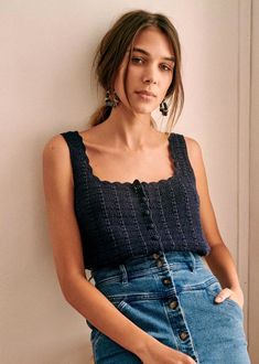 a woman leaning against a wall wearing a denim skirt