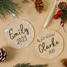 two personalized christmas ornament hanging on a table with pine cones and decorations