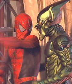 two men dressed in costumes standing next to each other near a building with spider - man on it