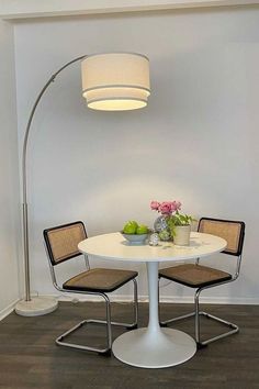 a white table with two chairs and a lamp in the corner next to it on top of a hard wood floor