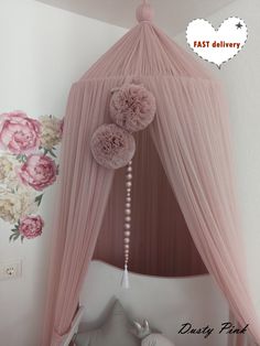 a pink canopy bed with pom poms hanging from it's sides and flowers on the wall