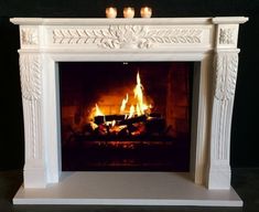 a white fireplace with flames burning in it's mantle and two candles on top