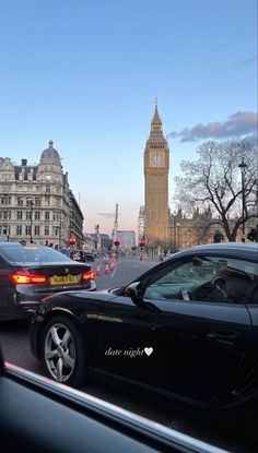 some cars are driving down the street in front of big ben and other tall buildings