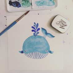 a watercolor painting of a blue whale on a white paper next to some paintbrushes