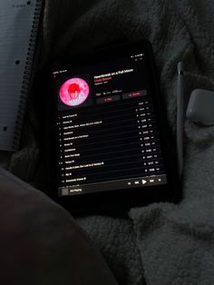 an electronic device sitting on top of a bed next to a notepad and pen