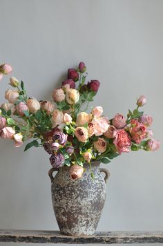 a vase filled with lots of flowers on top of a wooden table next to a wall