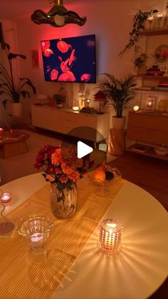 a table with flowers and candles on it in front of a television screen that is turned on