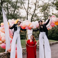 two women and a man are standing in front of an arch with balloons on it