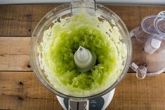 a food processor filled with green vegetables on top of a wooden table