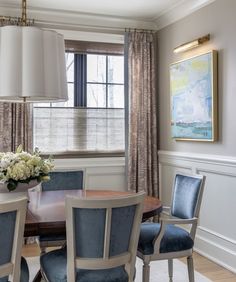 a dining room table with blue chairs and a painting hanging on the wall behind it