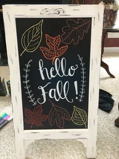 a chalkboard sign with the words hello fall written on it and leaves around it