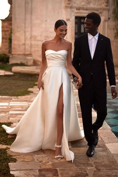 a man and woman in formal wear walking next to each other on a stone walkway