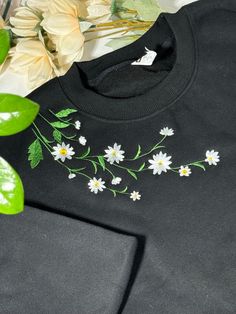 a black shirt with daisies and leaves on it next to a flower potted plant