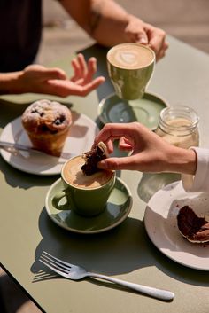 two people sitting at a table with cups of coffee and pastries in front of them