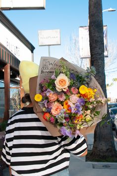 a woman holding a bouquet of flowers in front of her face while walking down the street