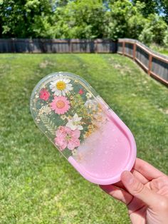 a hand holding a plastic container with flowers painted on the outside and inside, in front of a grassy area