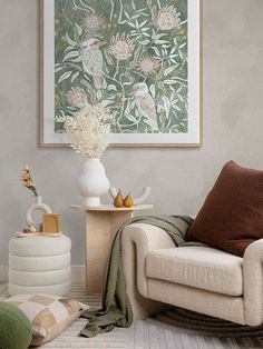 a white chair sitting next to a vase with flowers on it in front of a painting