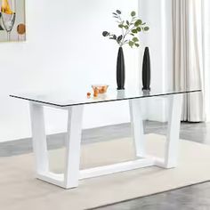 a glass table with two vases on it in front of a white wall and floor