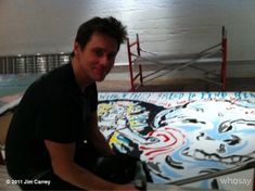 a man sitting in front of a skateboard with graffiti on the wall behind him