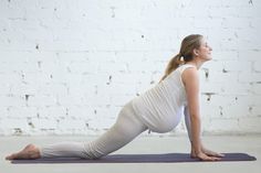 a pregnant woman is doing yoga in front of a white brick wall with her legs crossed