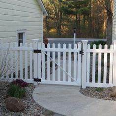 a white picket fence in front of a house with rocks and gravel on the ground