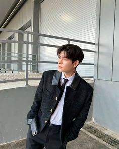 a young man wearing a suit and tie standing in front of a building with his hands in his pockets