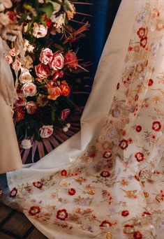 a white dress with red flowers on it next to a bouquet of pink and orange flowers