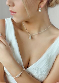 a woman in a white dress wearing a necklace and bracelet with pearls on the neck