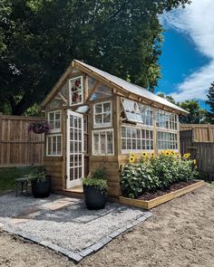 a small wooden house with lots of windows and plants in the front yard, next to a fence