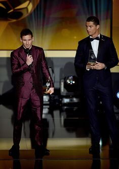 two men in tuxedos standing on stage at an awards event with one holding his award