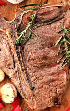 steak with rosemary garnish and garlic on a cutting board next to red peppers