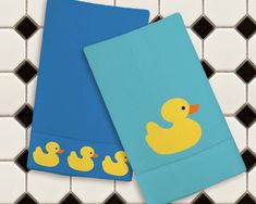 two towels with rubber ducks on them sitting next to each other in front of black and white tiles