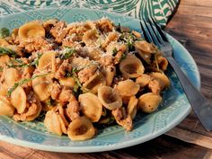 a blue plate topped with pasta and meat covered in sauce on top of a wooden table