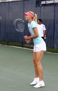 a woman standing on a tennis court with a racquet in her hand and people behind her